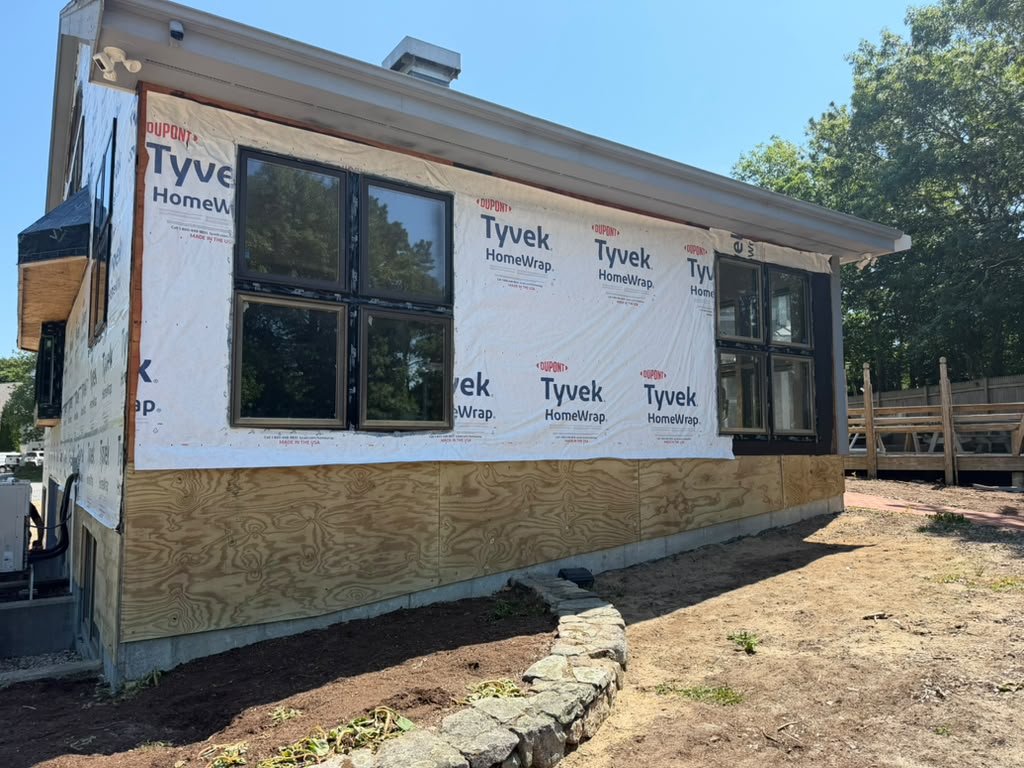 Home exterior with plywood sheathing and house wrap installed around new black windows